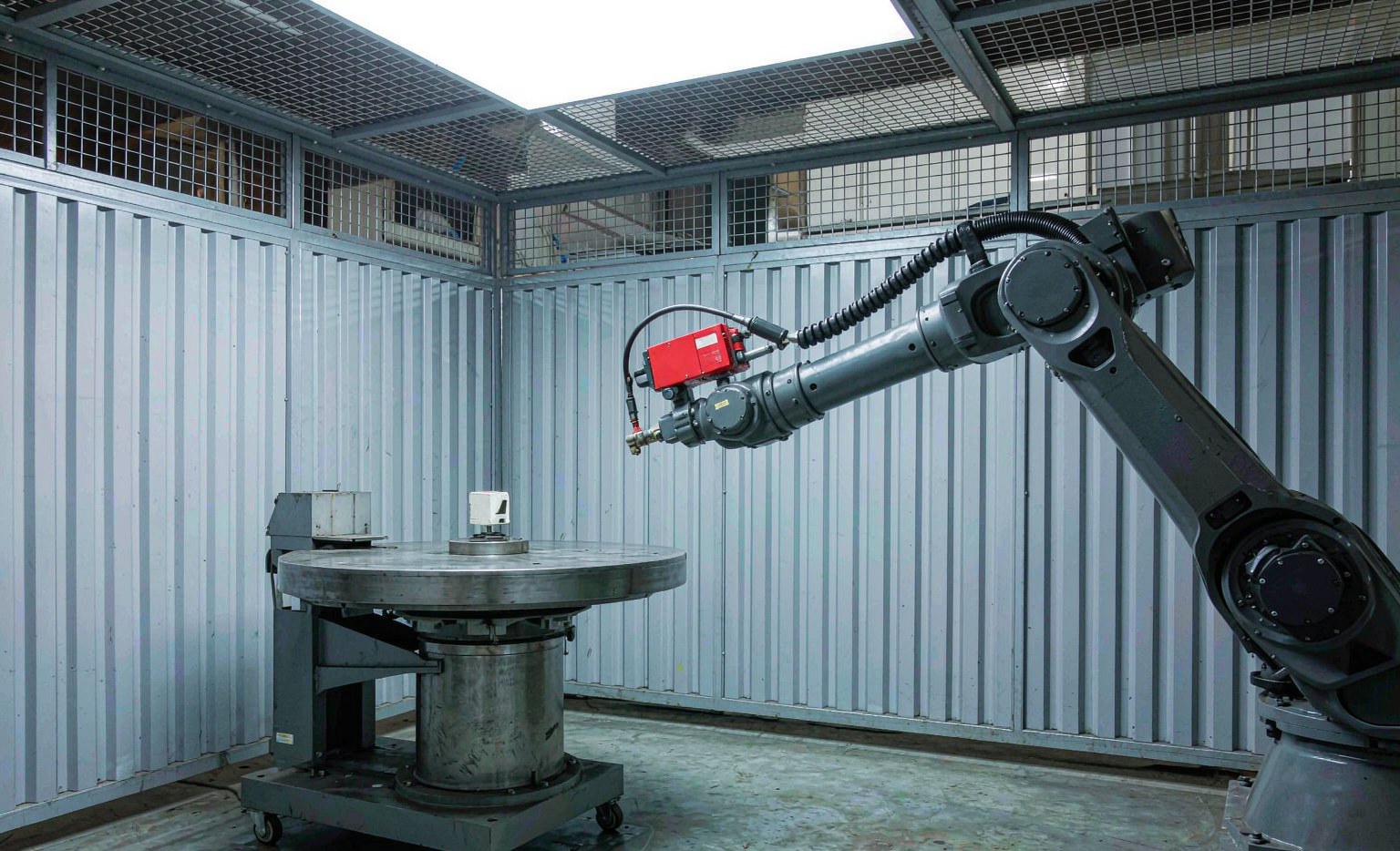 Six-axis welding robot inside a safety enclosure with positioner