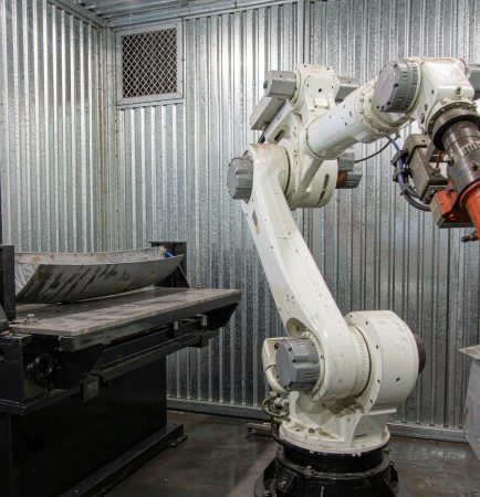 Six-axis welding robot inside a safety enclosure with positioner