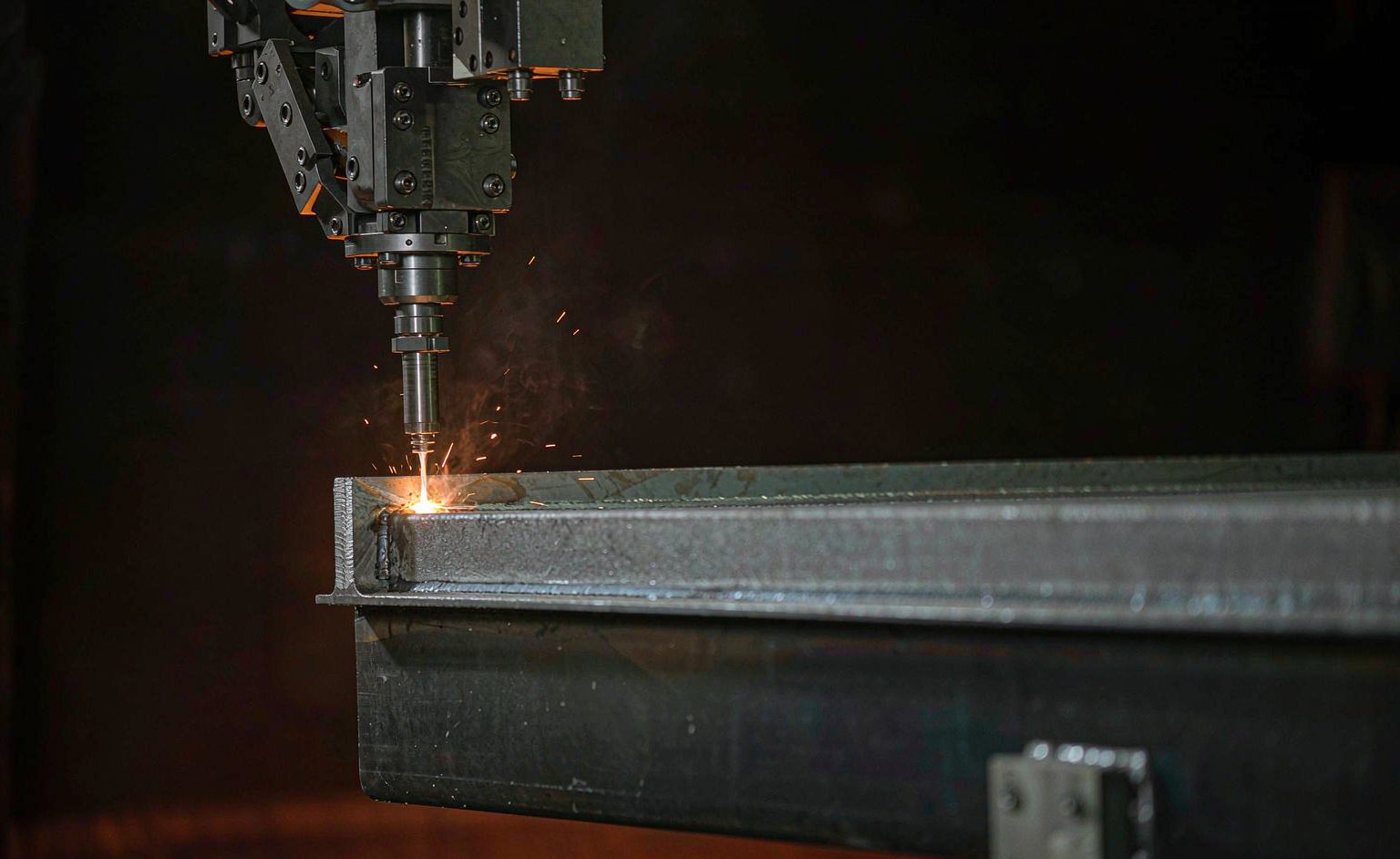 Integración del robot de soldadura láser FANUC: qué planificar antes de comprarlo Primer plano de una cabeza de soldadura láser en un brazo robótico que produce una junta de soldadura brillante sobre acero