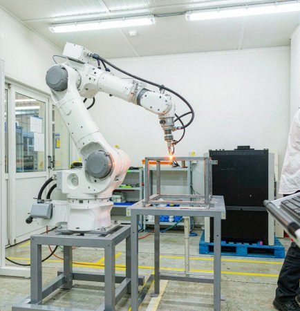 Brazo de robot colaborativo (cobot) soldando un marco de metal junto a un técnico en un taller moderno y limpio