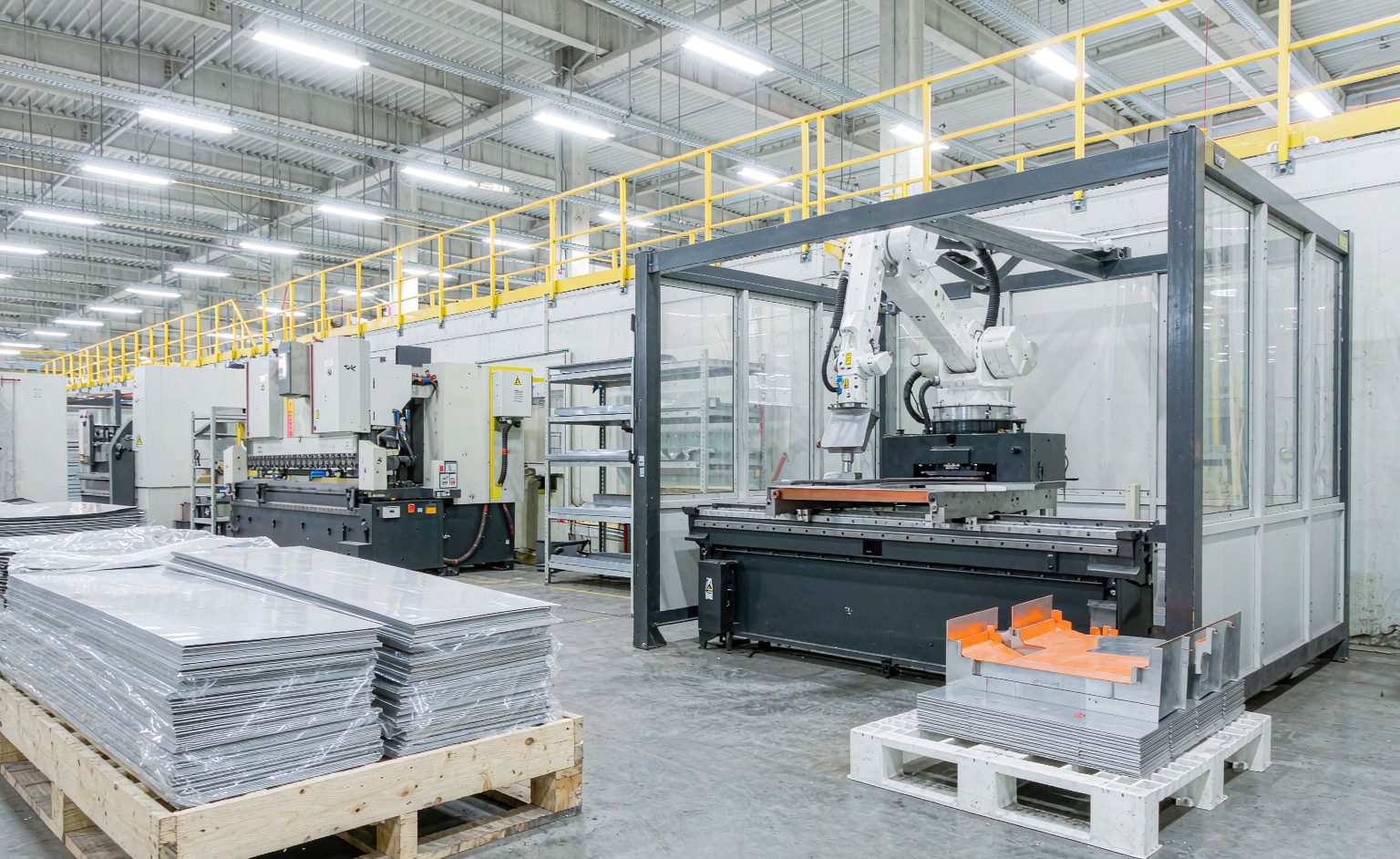 Bending and Forming Robots: Cell Design, Capabilities and ROI for Metal Fabricators → 금속 가공업체를 위한 벤딩 및 성형 로봇: 셀 설계, 기능 및 ROI 적층된 시트 메탈 블랭크와 완성된 성형 부품이 있는 로봇 프레스 브레이크 성형 셀의 와이드 뷰